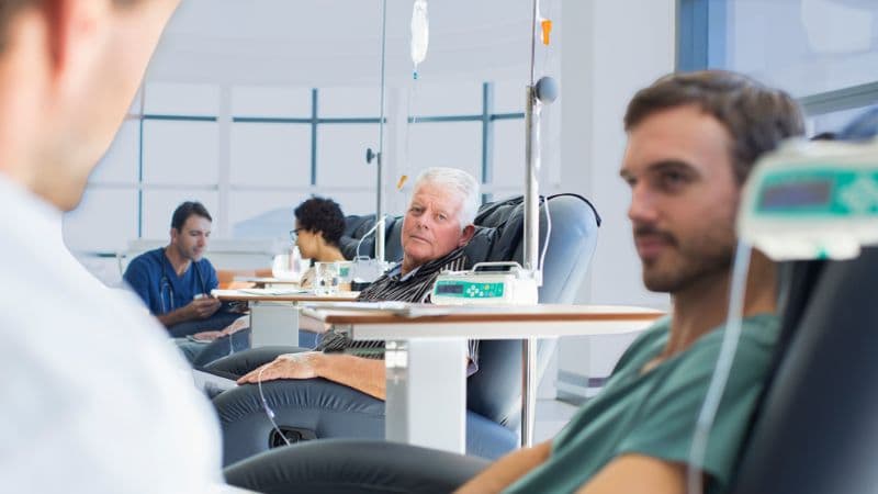 Doctors Talking To Patients Receiving Medical Treatment In Hospital Ward