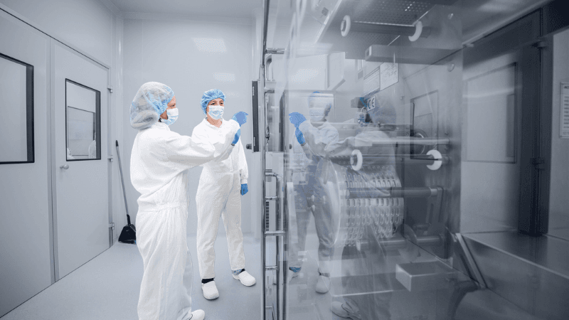 CDMO Professionals Reviewing Pharmaceutical Manufacturing Operations In A Cleanroom Environment.