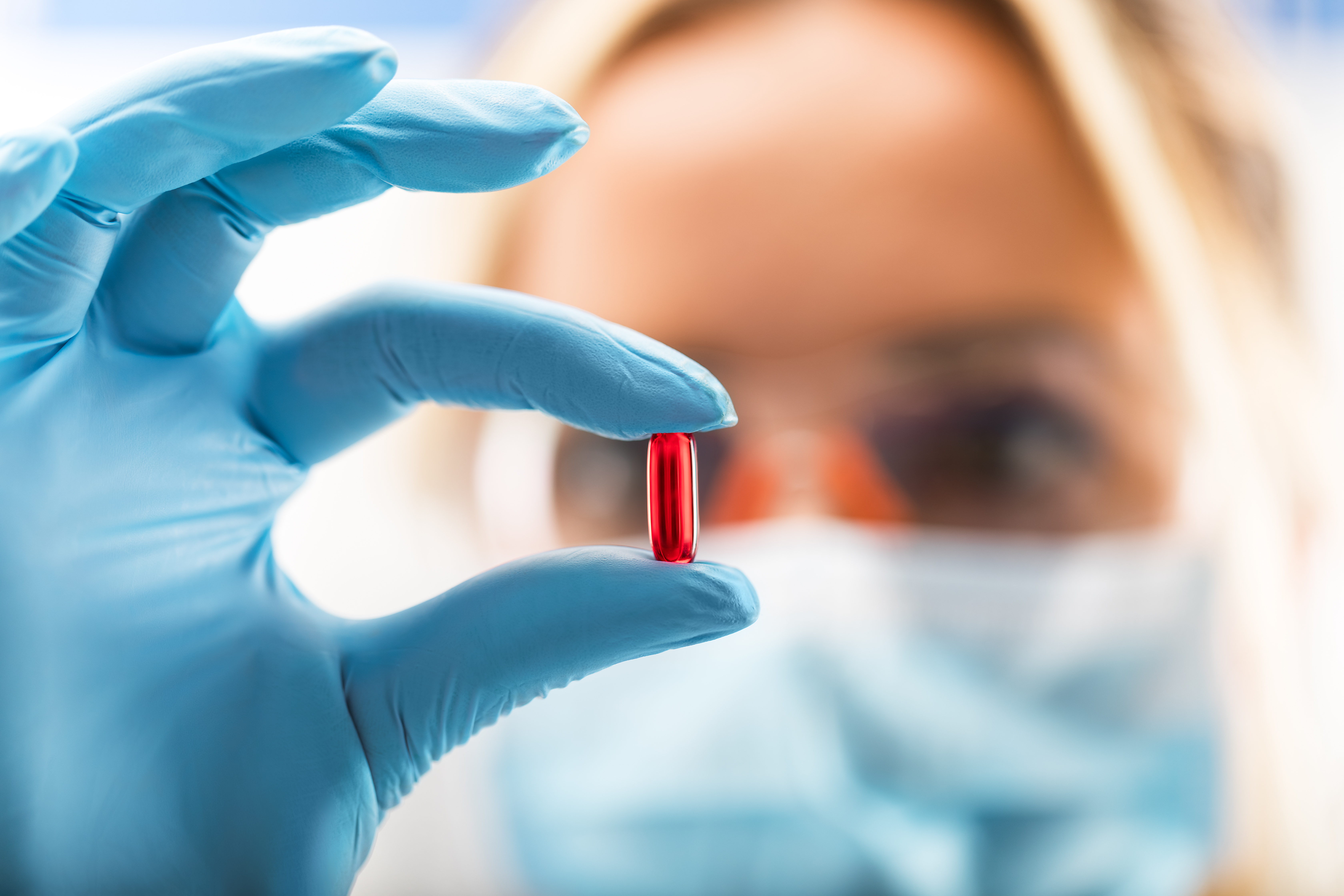 A woman scientist holding a red pill between her fingers with gloves on