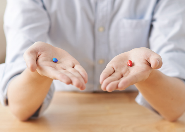 one hand holding a blue pill and the other holding a red pill