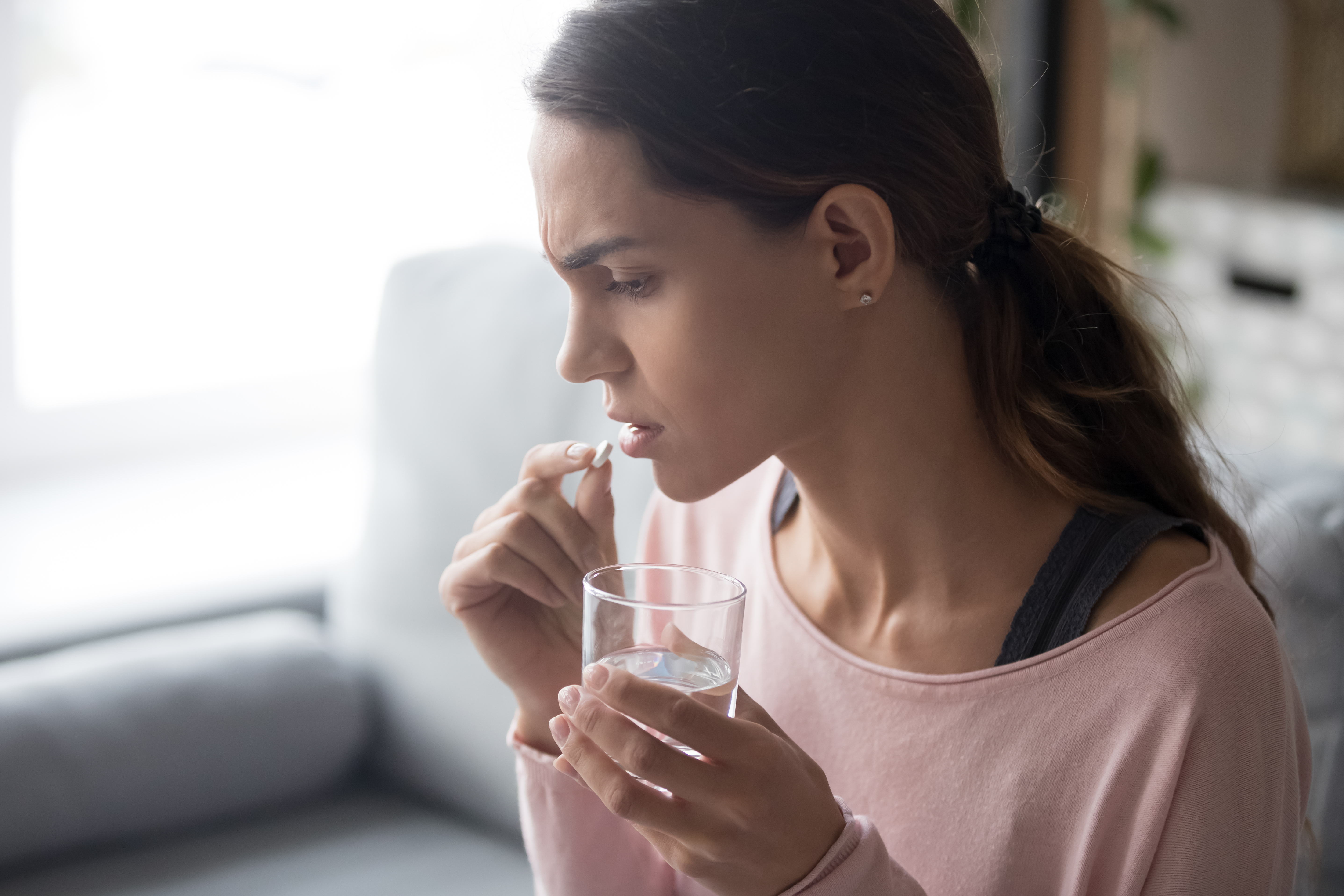 a picture of a woman taking a pill into her mouth and holding a glass of water