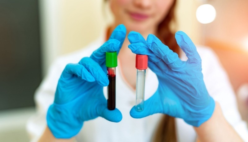 woman holding two vials, one with blood and the other is empty